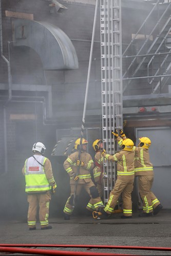 Firefighters carrying out a ladder drill at their pass out ceremony on 2nd December 2022, with the Incident Commander overseeing the exercise.